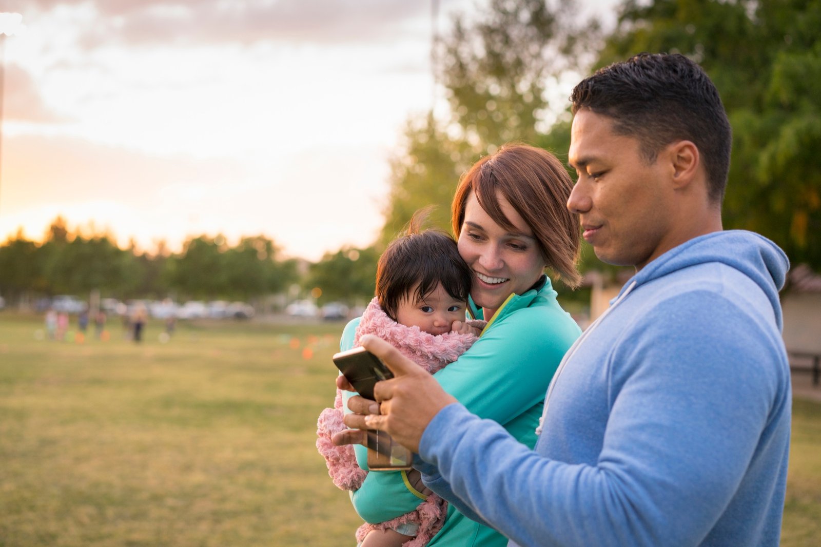 Couple with baby, using mobile phone in park